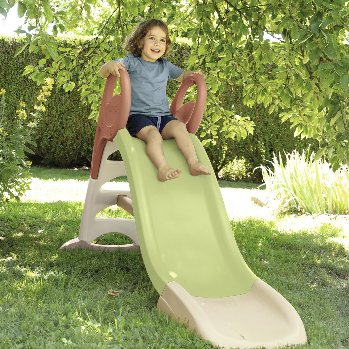 Child on lime green and burgundy plastic slide in outdoor garden setting