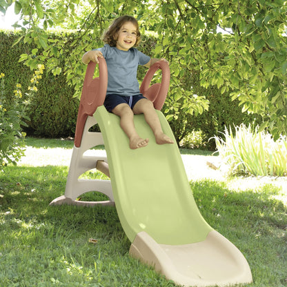 Child on lime green and burgundy plastic slide in outdoor garden setting