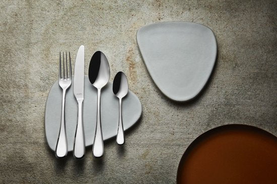 Amefa Drift stainless steel flatware set with four-piece place setting and white plates on grey surface