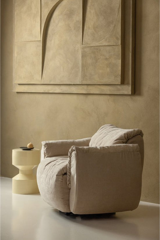 Beige upholstered curved armchair with cream pillows and cylindrical yellow metal side table